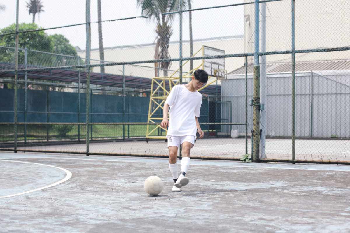 Joven jugando fútbol en cancha exterior.